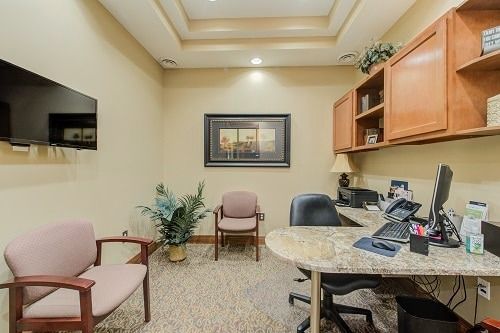 Office with desk, chairs, TV, and cabinets; beige walls and carpet.