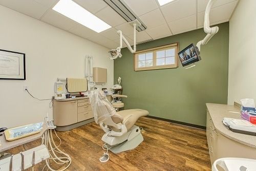 Dental operatory with chair, equipment, wood floor, and sage green accent wall.
