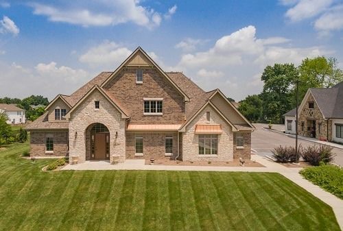 Brick home with a large arched entrance, copper accents, and well-manicured lawn on a sunny day.