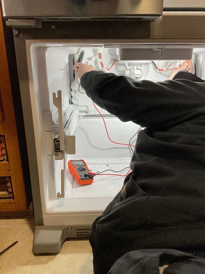 A man is working on a refrigerator with a multimeter.