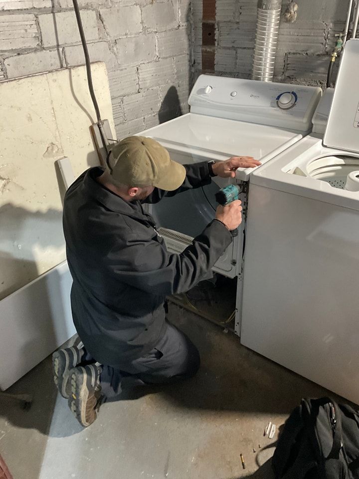 A man is fixing a washer and dryer in a basement.