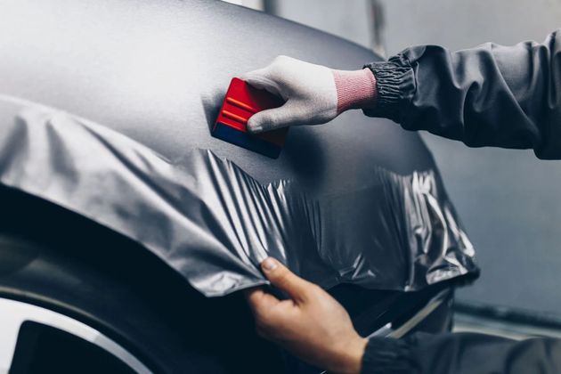 Hands applying a red squeegee to smooth silver car wrap on a vehicle body