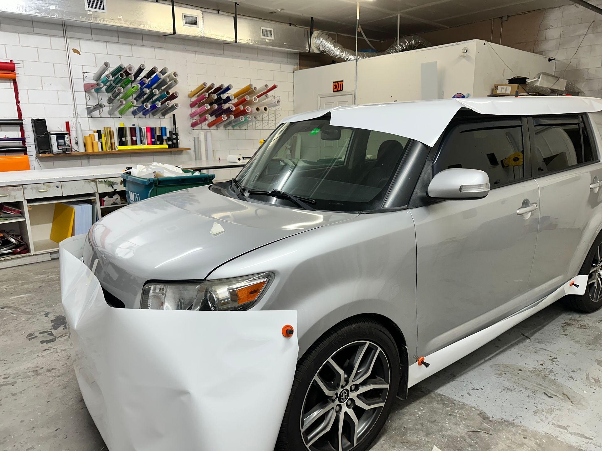 Silver SUV parked in a workshop, covered with a white protective sheet on the front.