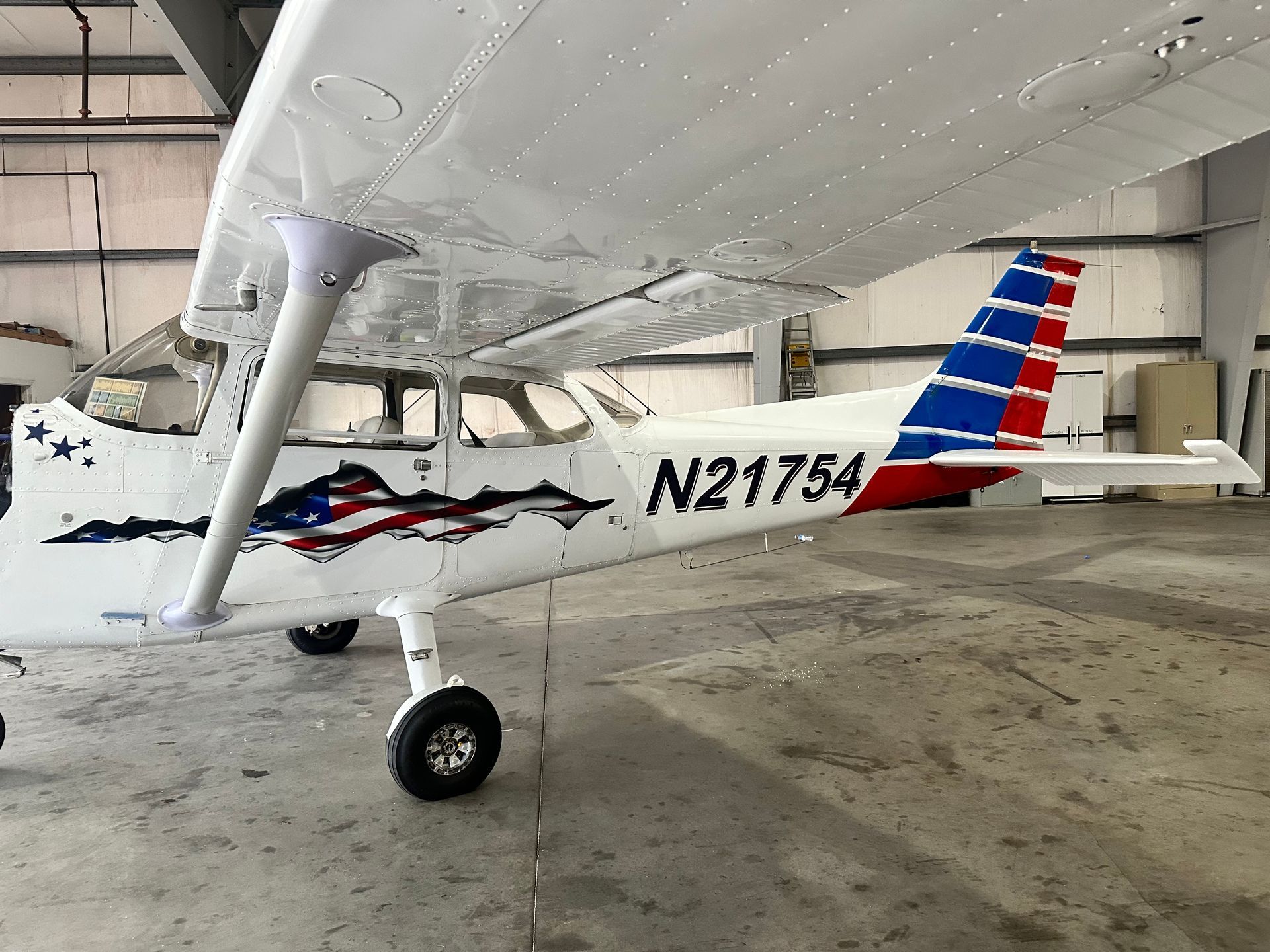 Small white single-engine airplane with red and blue stripes parked inside a hangar
