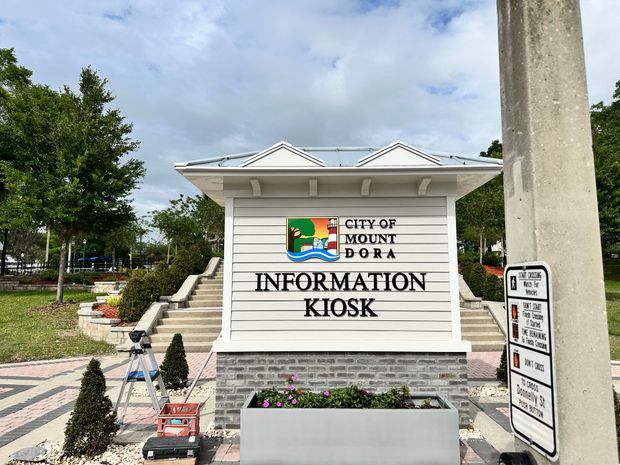 City of Norco information kiosk sign with white siding, green roof, and stairs outside on a sunny day