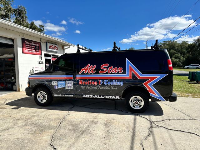 Black service van with red-and-white star logo parked outside a shop on a sunny day