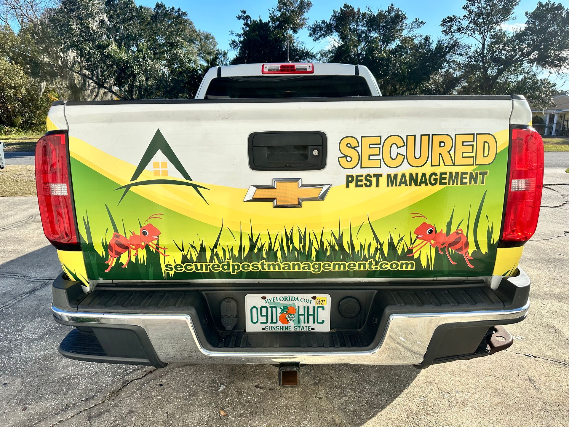 Pickup truck tailgate with Secured Pest Management logo, yellow grass graphic, and Florida license plate.