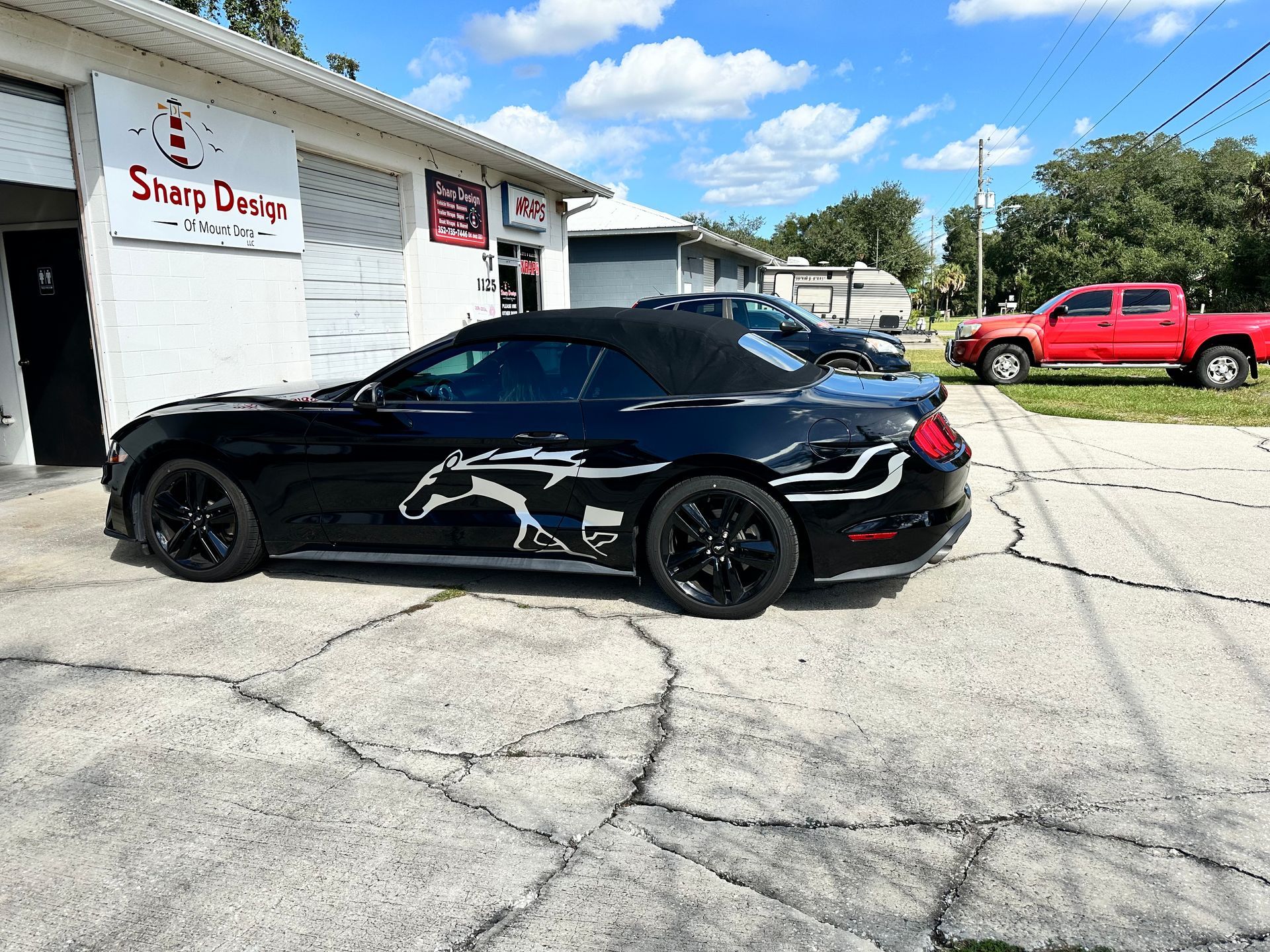Black sports coupe with horse decal parked outside a shop on a sunny day