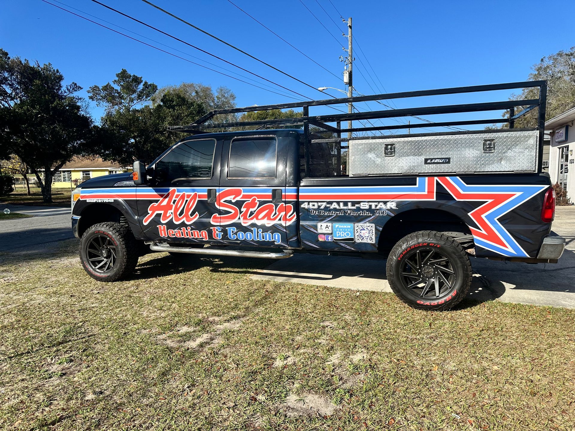 Lifted black pickup truck with red and blue racing graphics parked on grass under a clear blue sky