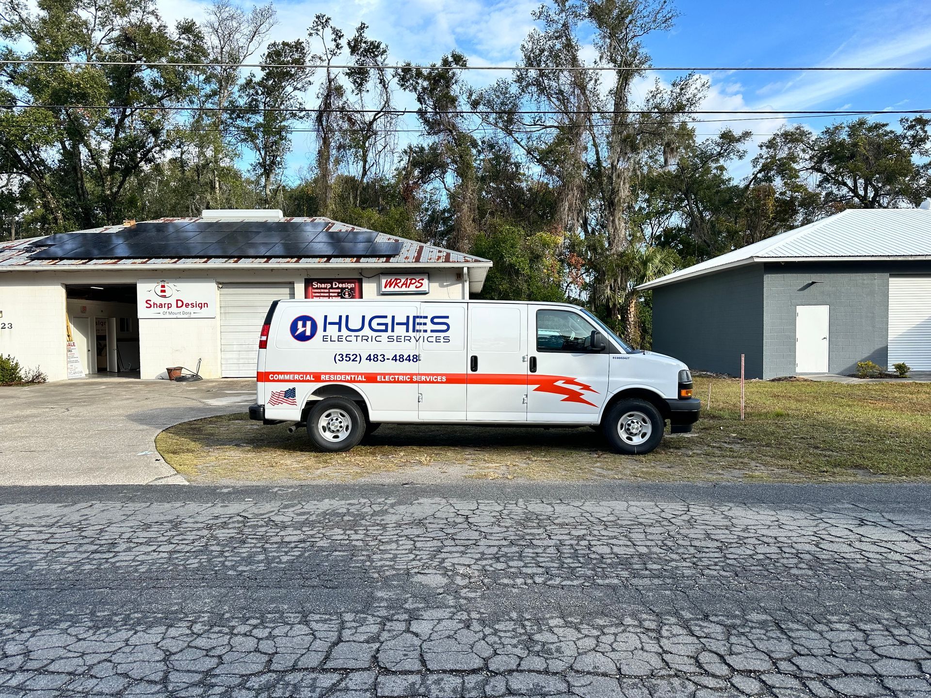 White utility van with red stripe parked beside a rural building and gravel road.