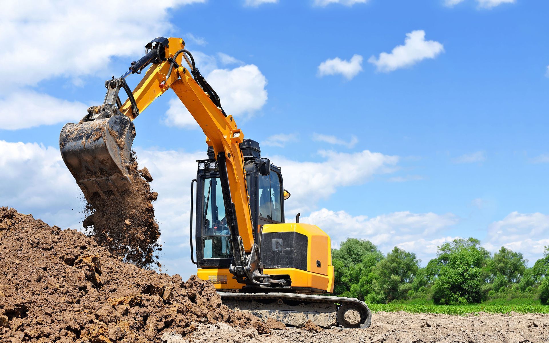 a yellow excavator is digging a pile of dirt in a field