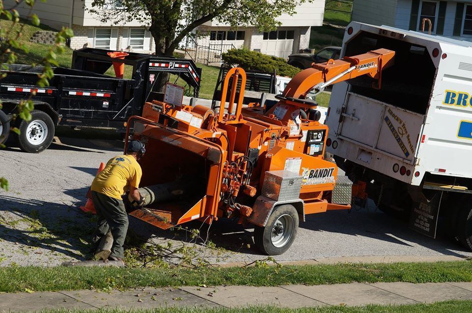Worker loading branches into orange wood chipper beside white truck on a residential street