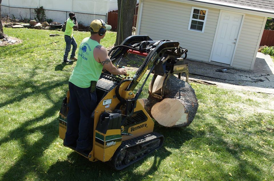 Worker using a yellow mini loader to move a large rock in a backyard beside a house