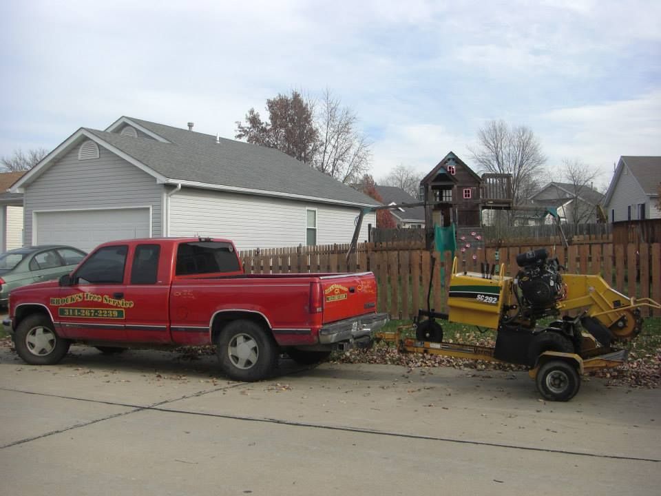 Red pickup truck parked by a yellow wood chipper on a suburban street with houses behind.