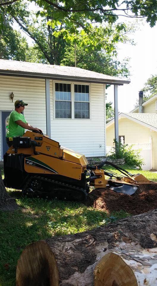 Person operating a yellow skid steer beside a white house, digging a muddy yard area.