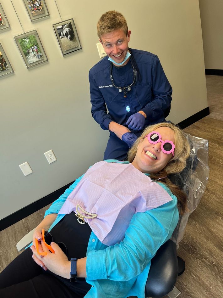 A woman is sitting in a dental chair with a dentist standing behind her.