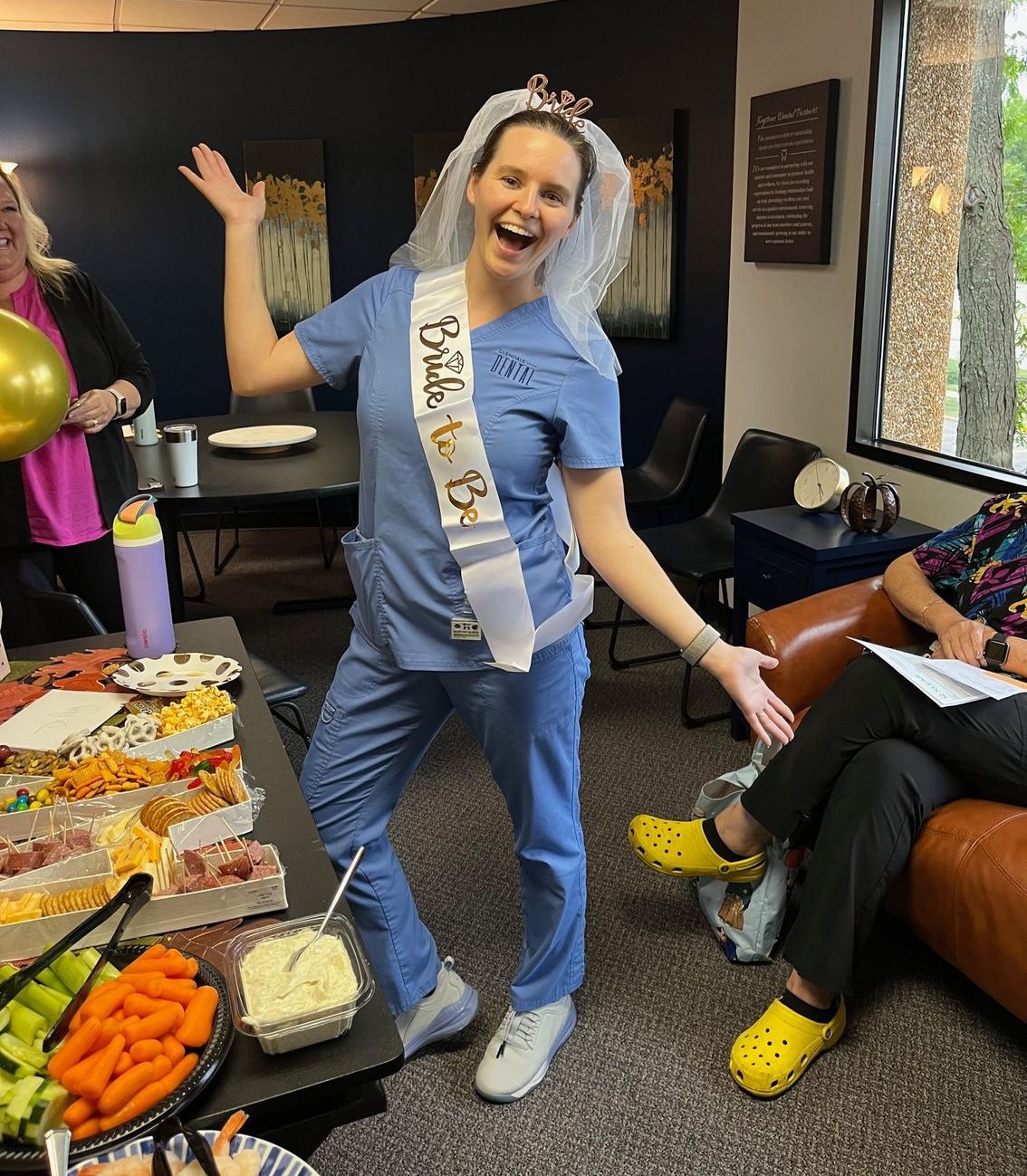 A woman in scrubs is wearing a sash that says bride to be.
