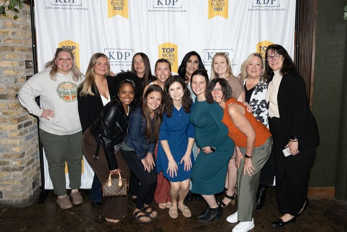 A group of women are posing for a picture in front of a wall.