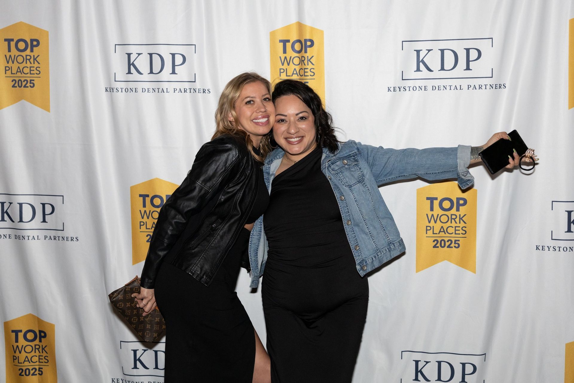 Two women are posing for a picture in front of a backdrop.