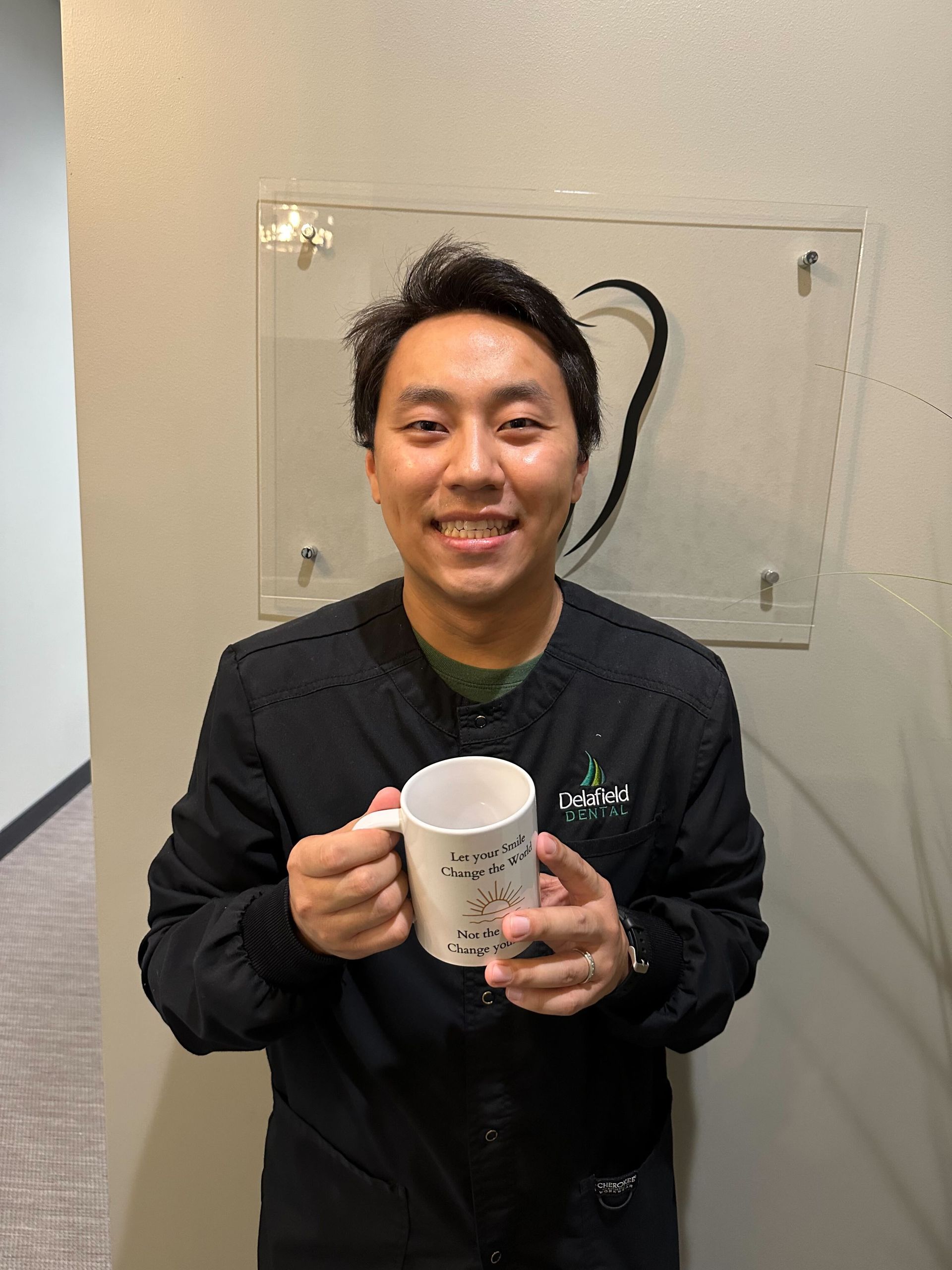 a man in a black jacket is holding a mug in front of a wall