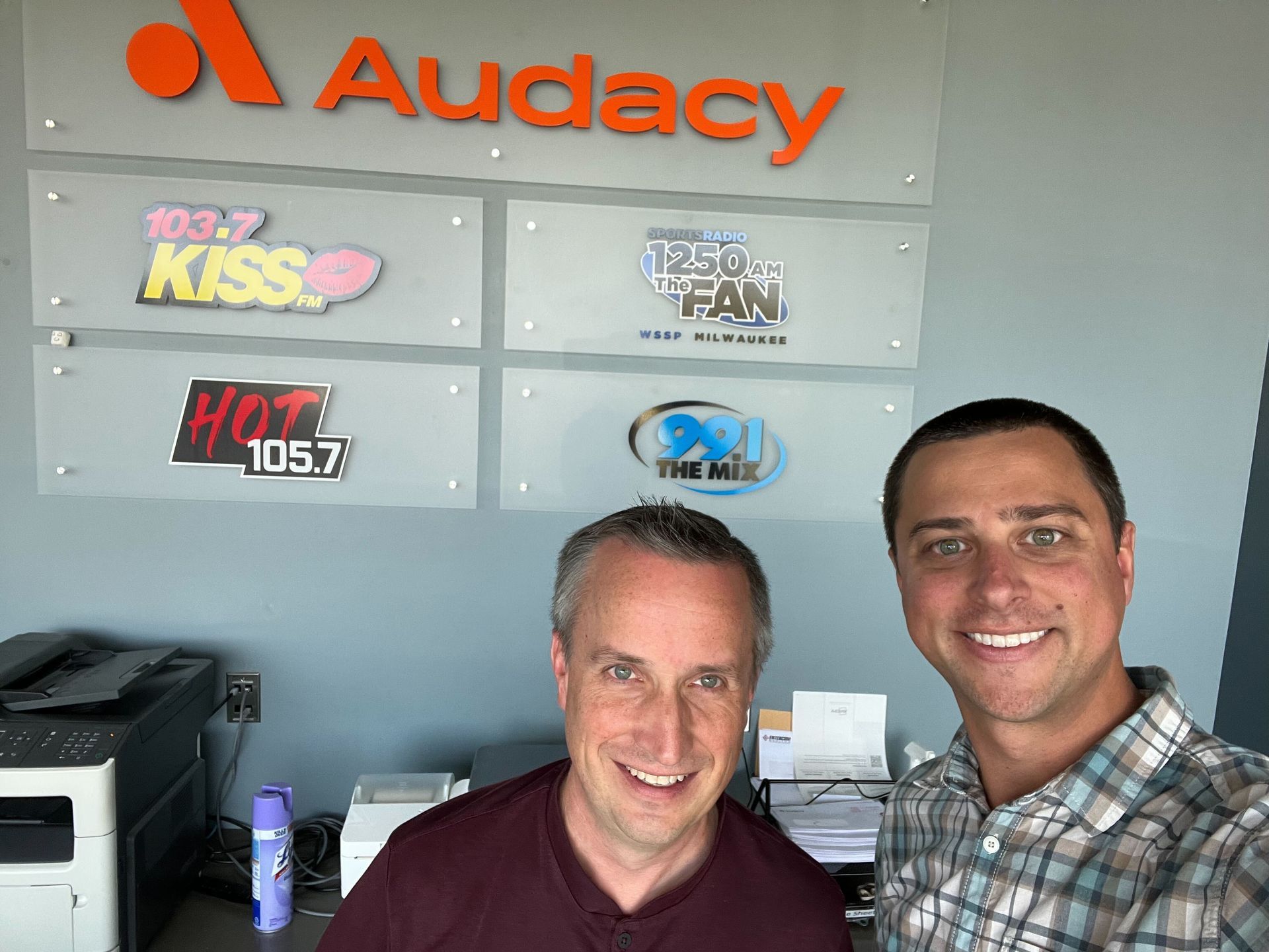 two men are standing in front of a sign that says audacy