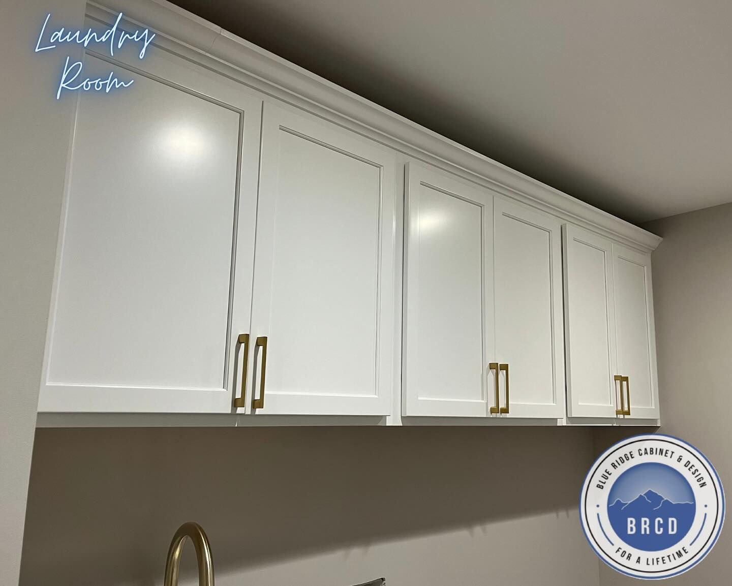 A laundry room with white cabinets and gold handles