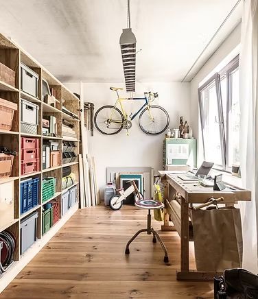 A room with a bicycle hanging from the ceiling and a desk.