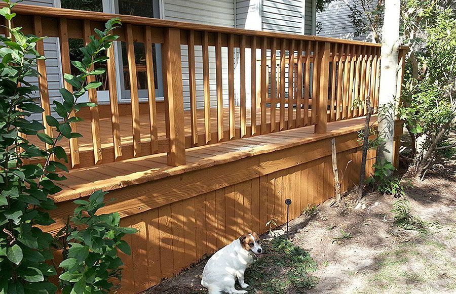 A dog is sitting on the side of a wooden deck.