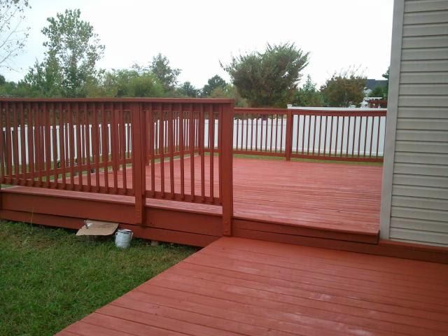 A red deck with a white railing and a white house