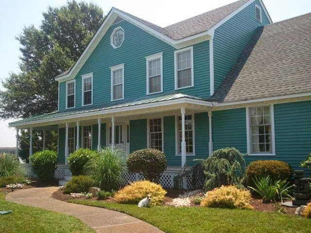 A large green house with a porch and lots of windows