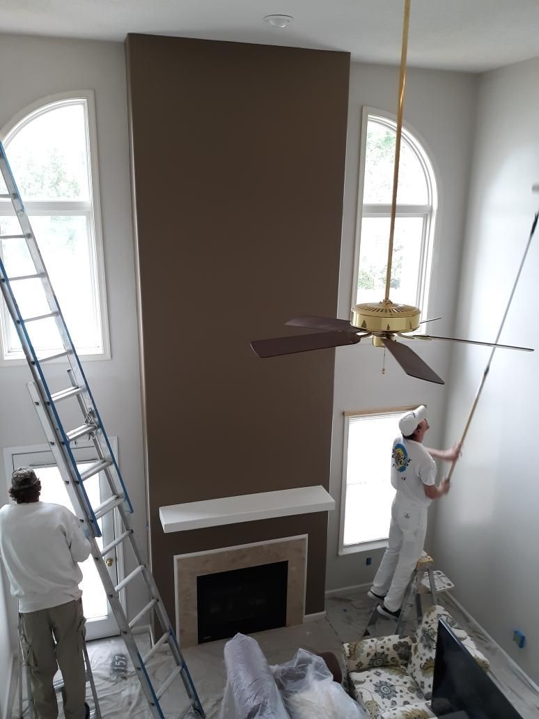 Two men are painting a living room with a fireplace and a ceiling fan