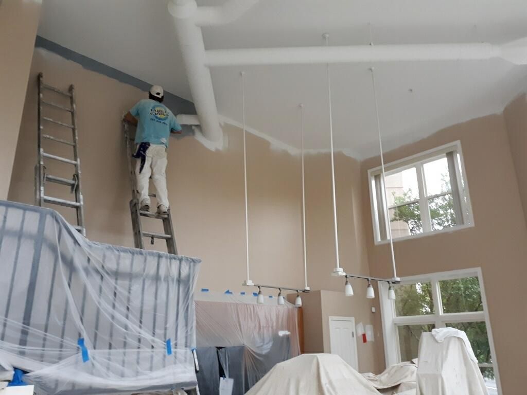 A man is standing on a ladder painting the ceiling of a room