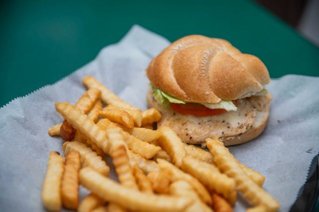 Hamburger on bun with lettuce and tomato, next to a pile of crinkle-cut fries on a white paper.