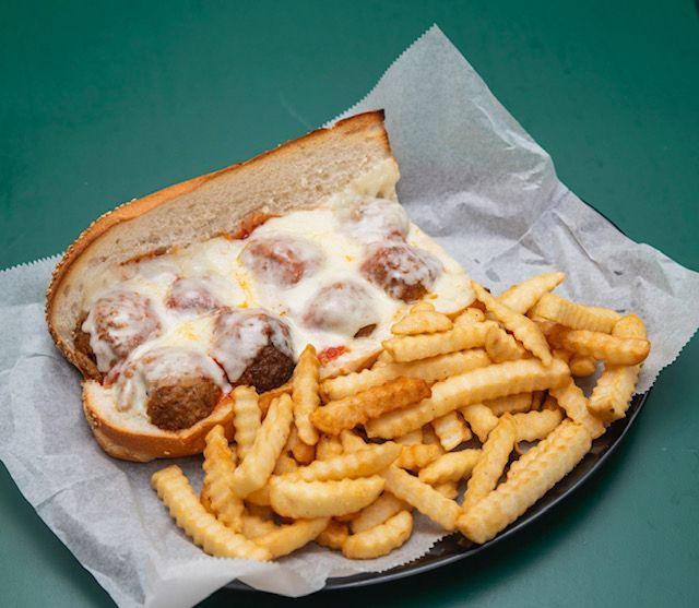 Meatball sub with melted cheese and crinkle-cut fries on a plate with parchment paper.