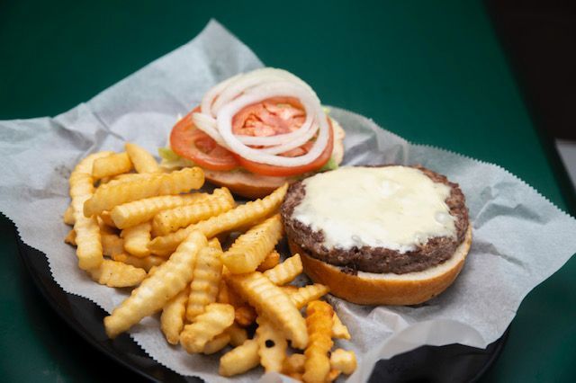 Hamburger with crinkle-cut fries on a plate with toppings of tomato and onion.