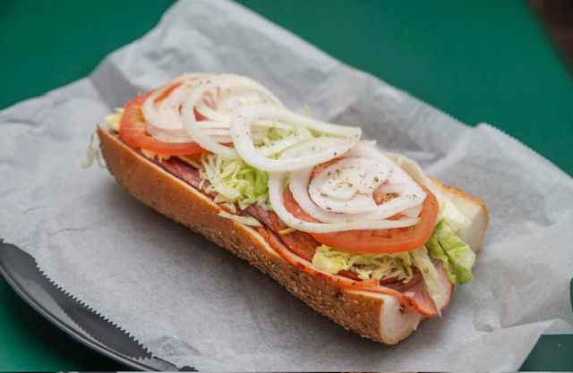 Sub sandwich on parchment paper: bread, meat, lettuce, tomato, and onion.