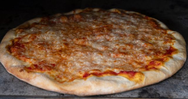 Pizza with melted cheese, inside a dark oven.