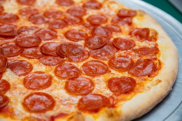 Pepperoni pizza on a metal tray, with a golden crust and lots of round, red pepperoni.