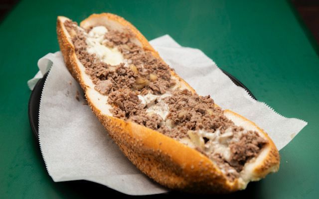 Philly cheesesteak sandwich on a white paper on a green surface.