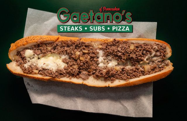 Large sandwich filled with ground meat and cheese, presented on a white paper, with the restaurant's logo.