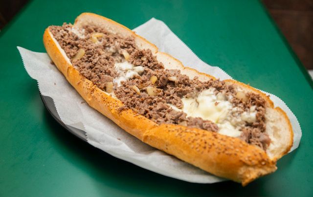 Philly cheesesteak sandwich on a white paper liner, atop a green surface.