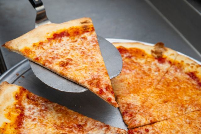 Slice of cheese pizza being lifted from a pie with a metal spatula.