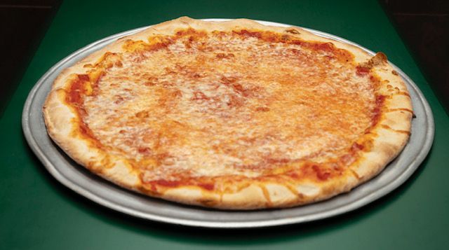 Cheese pizza on a metal pan, on a green table.