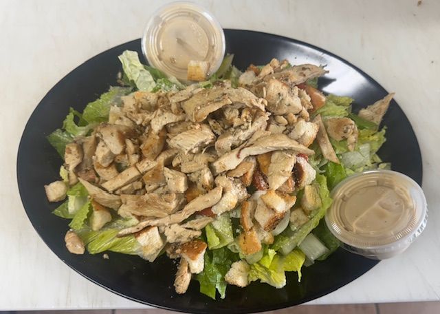 Chicken Caesar salad with dressing, served on a black plate.
