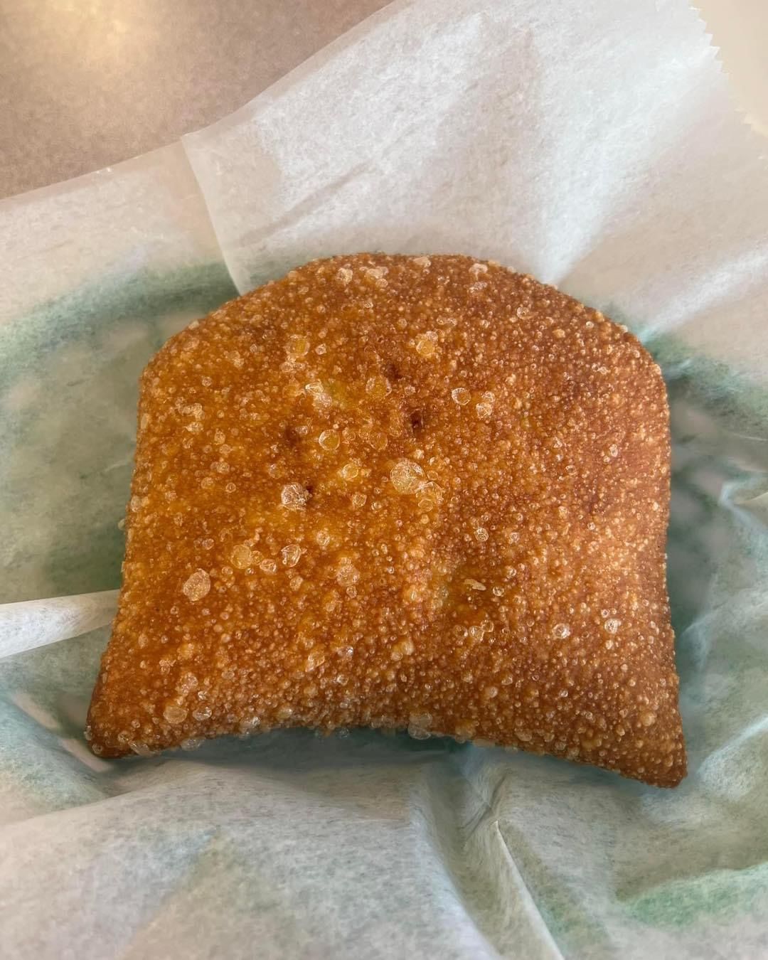 Golden-brown, fried, rectangular pastry, nestled in a white and green paper basket.