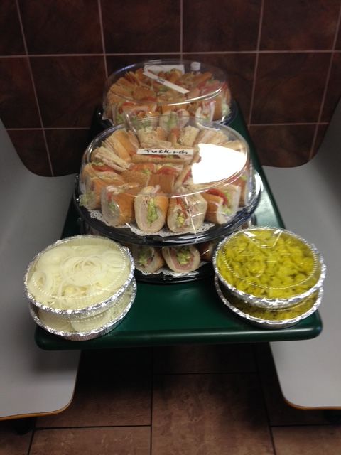 Platters of sandwiches and appetizers on a green table, in a brown-tiled room.