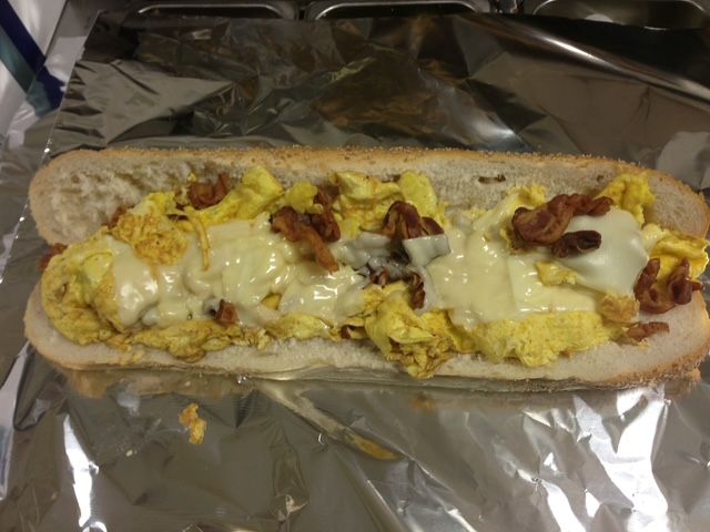 Sub sandwich with scrambled eggs, bacon, and melted cheese on aluminum foil.