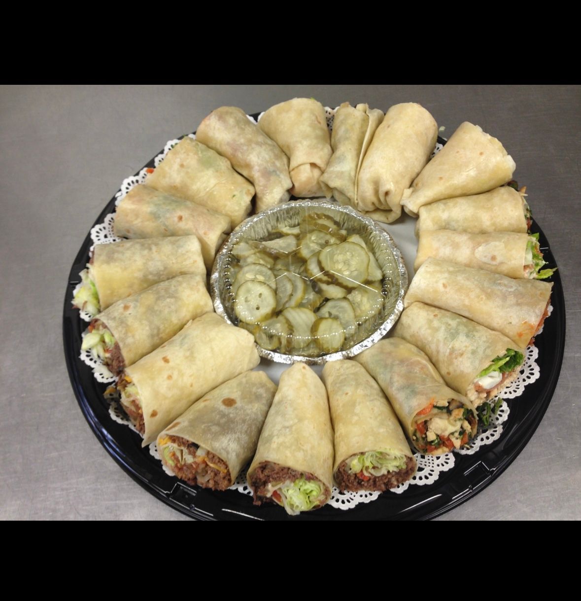 Wraps arranged on a platter around a container of pickles.