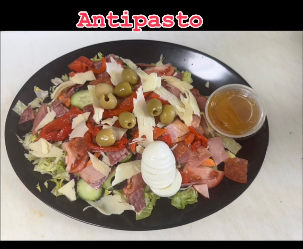 Antipasto salad: lettuce, cured meats, cheese, olives, hard-boiled egg, dressing, on black plate.