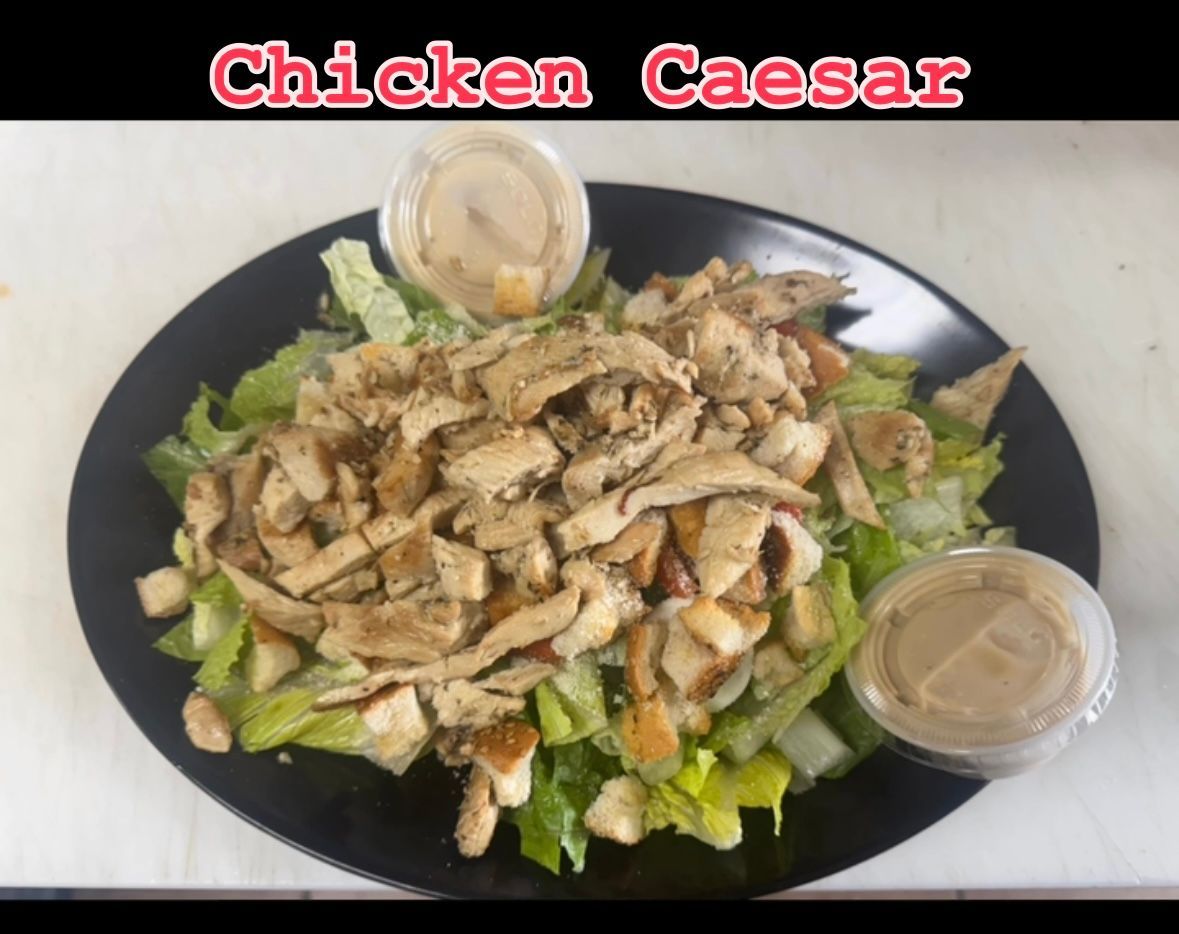 Chicken Caesar salad on black plate, with dressing in small containers.